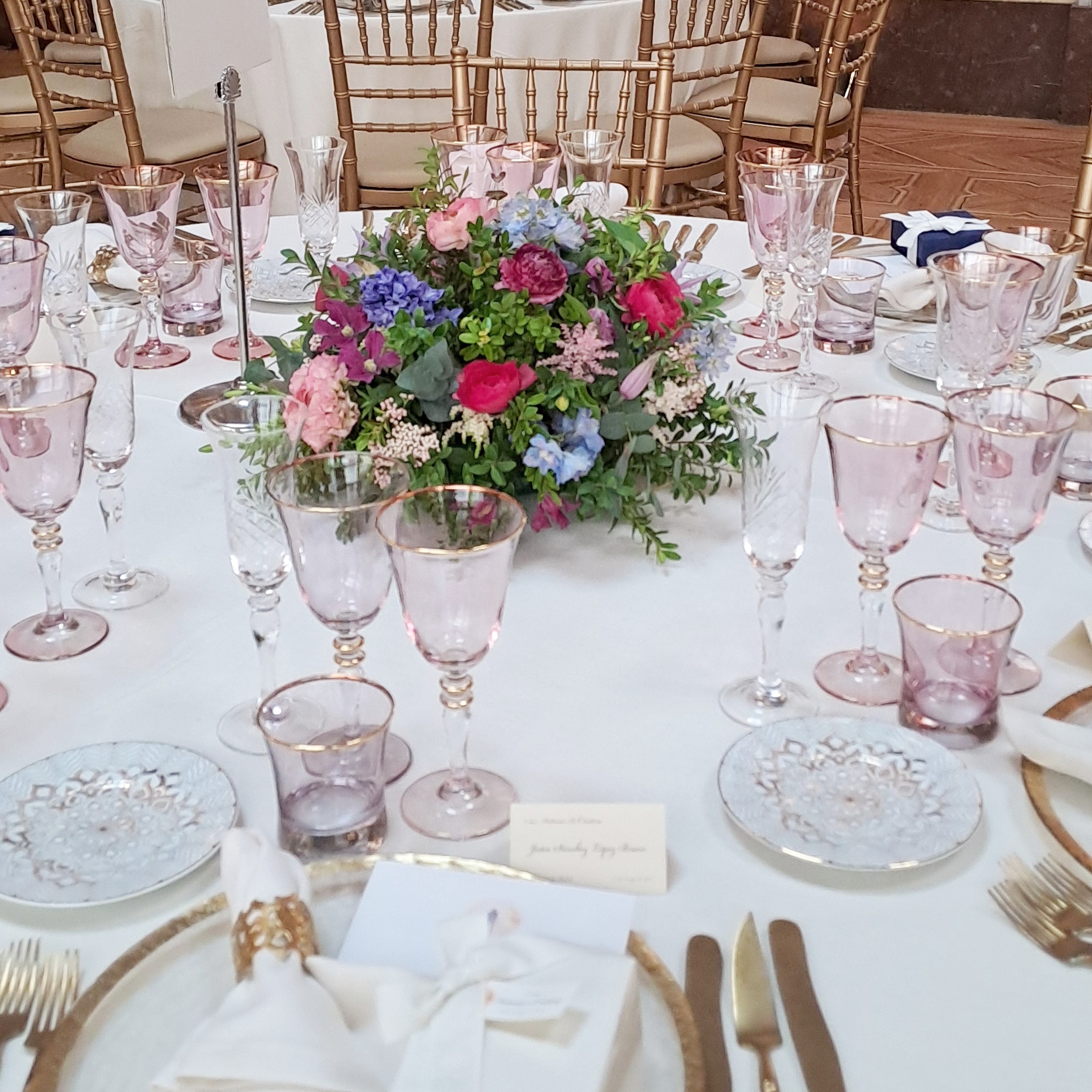 Centro floral en tonos rosa, fucsia y azul sobre mesa de banquete
