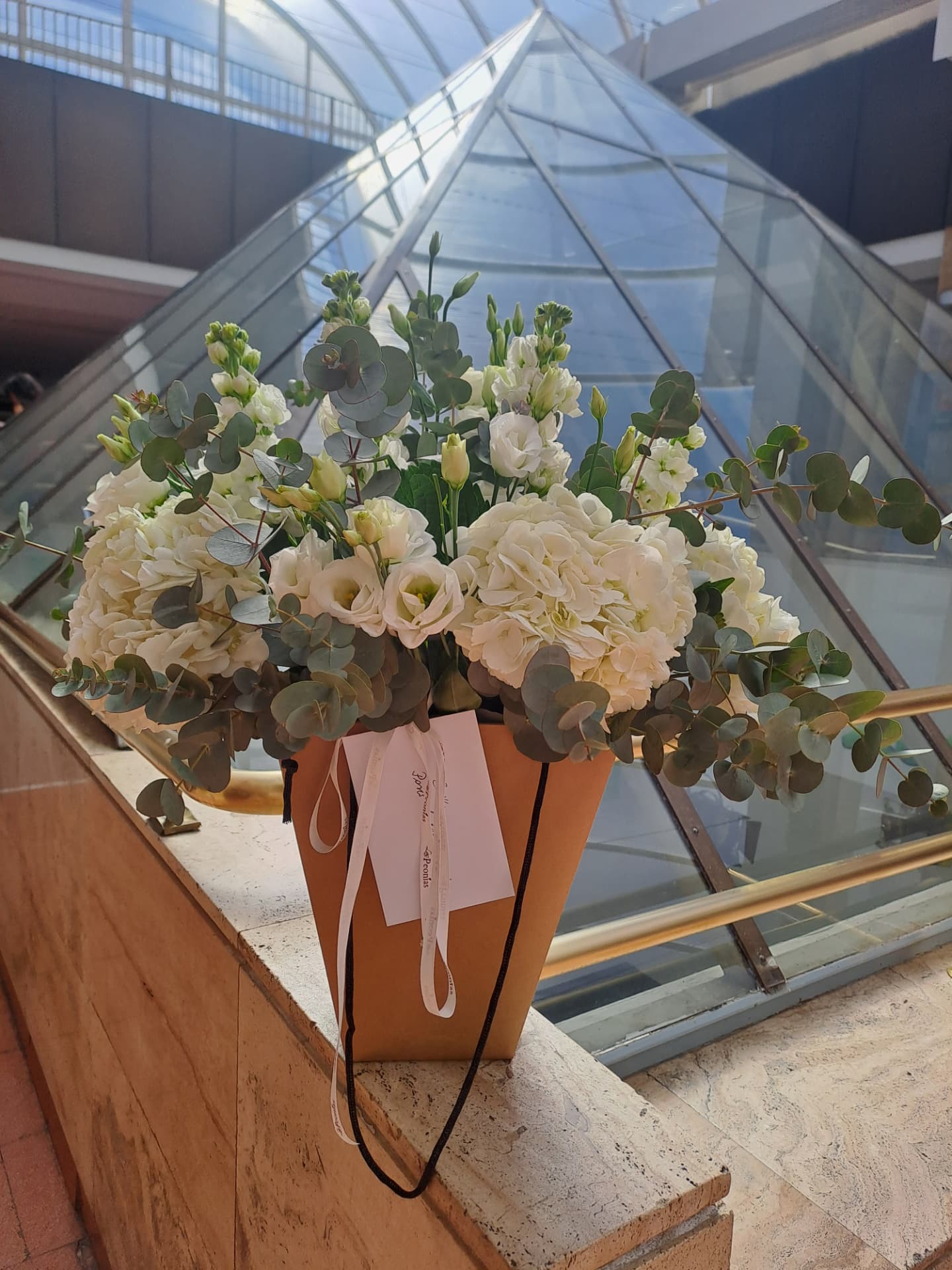 Centro floral blanco con hortensia, lisianthus y eucalipto en bolsa de papel