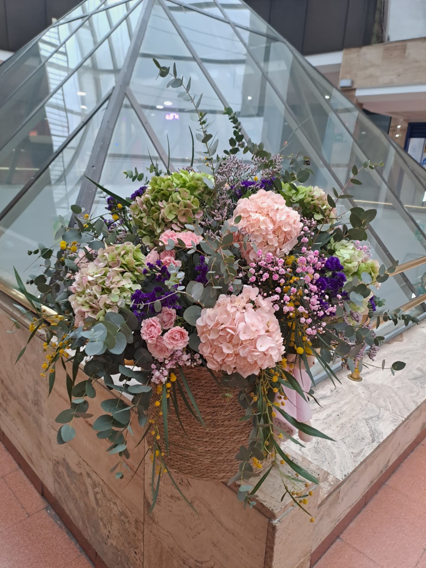 Centro floral en cesta con hortensias rosas, mimosa y eucalipto