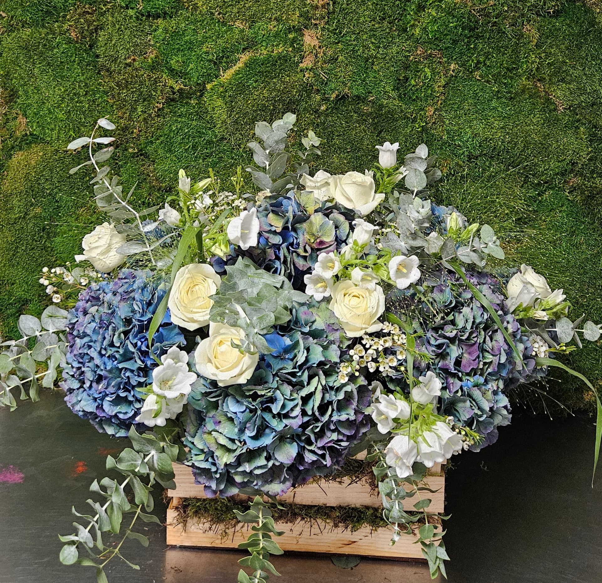 Centro floral con hortensias azules y rosas blancas sobre caja de madera