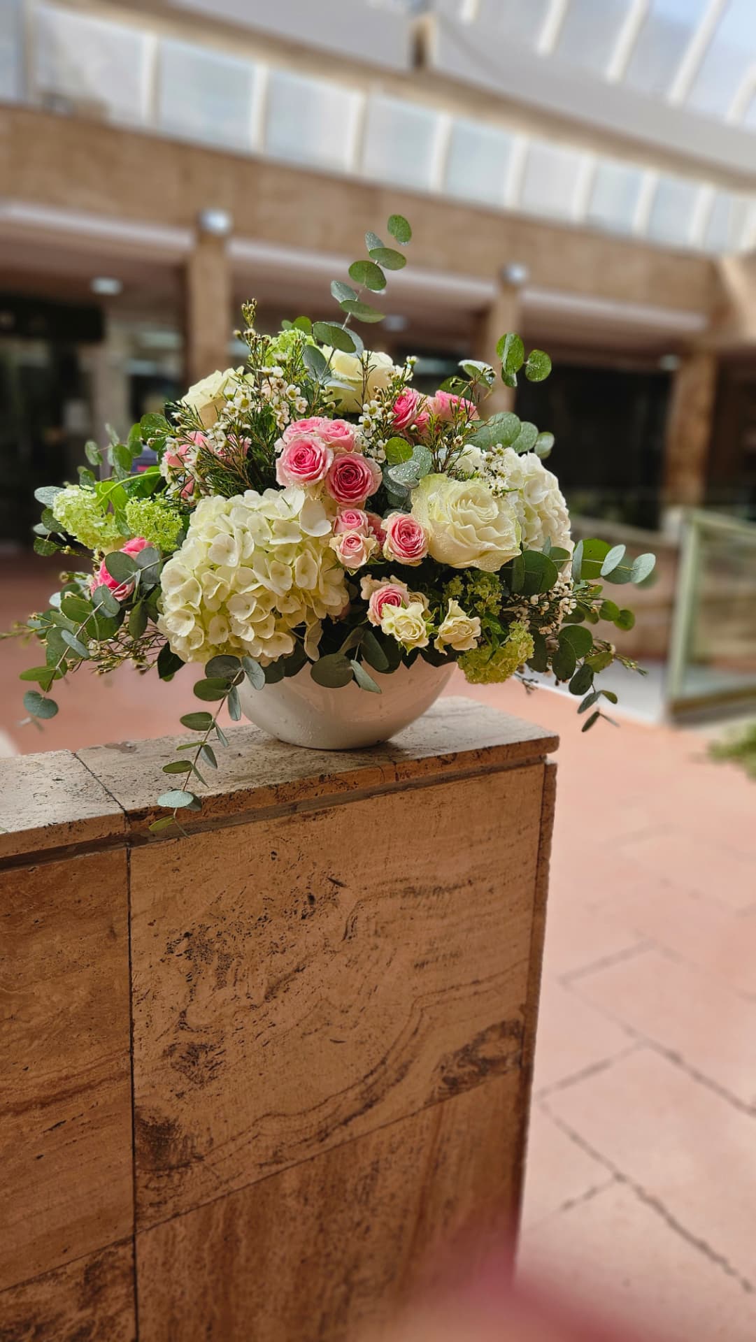 Centro bajo en cuenco blanco con hortensia, rosas rosas y eucalipto