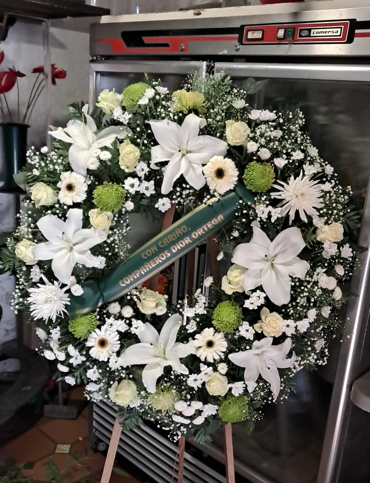 Corona funeraria de lilium blanco, rosas y paniculata con cinta verde