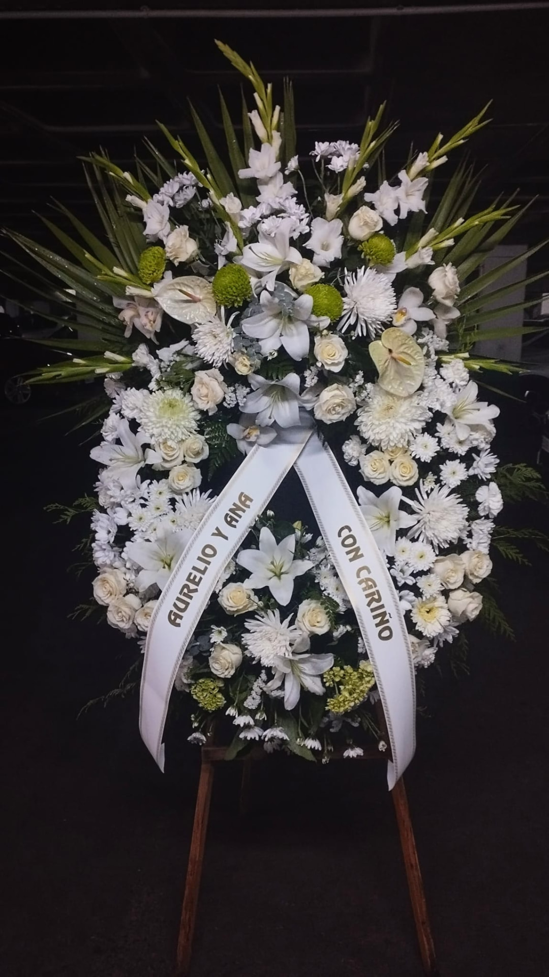 Palma funeraria de flor blanca sobre caballete con cinta de dedicatoria